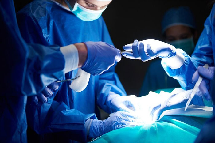 Surgeons in blue scrubs perform surgery under bright lights. Surgeons in blue scrubs perform surgery under bright lights.