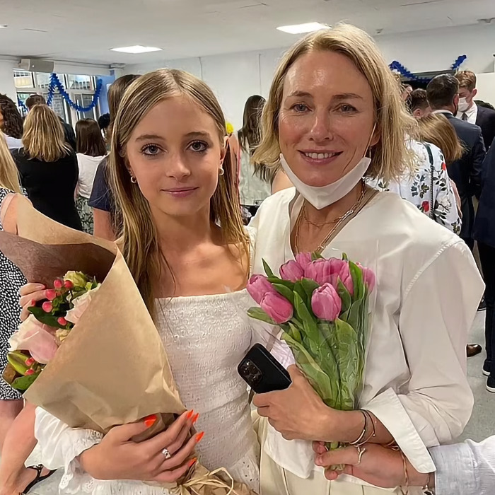 Mother and daughter holding flowers, posing together at an indoor event. Mother and daughter holding flowers, posing together at an indoor event.