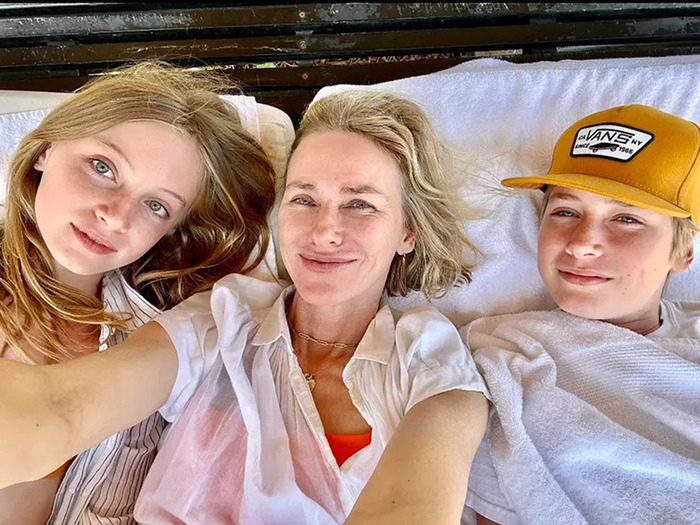 Naomi Watts with her two children, smiling while lying down together outdoors. Naomi Watts with her two children, smiling while lying down together outdoors.
