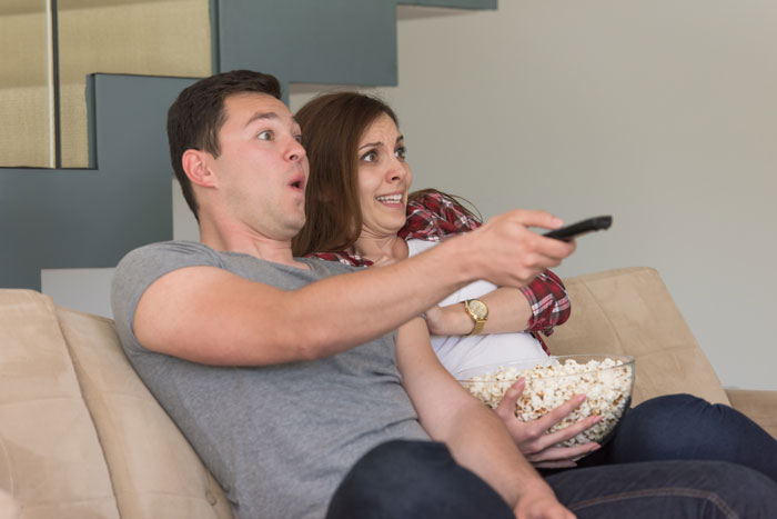 A surprised couple on the couch with popcorn, reacting to noise from neighbors treating the building like a nightclub. A surprised couple on the couch with popcorn, reacting to noise from neighbors treating the building like a nightclub.