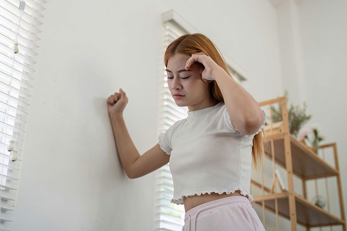 Woman frustrated with noise complaints, leans against wall, eyes closed, in a room with plants and shelves. Woman frustrated with noise complaints, leans against wall, eyes closed, in a room with plants and shelves.