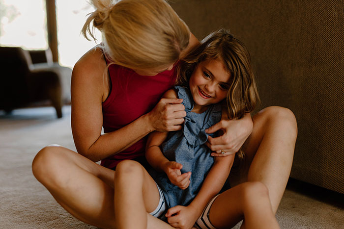 A mother playfully hugs her young daughter on the floor, highlighting the fragile nature of early childhood. A mother playfully hugs her young daughter on the floor, highlighting the fragile nature of early childhood.