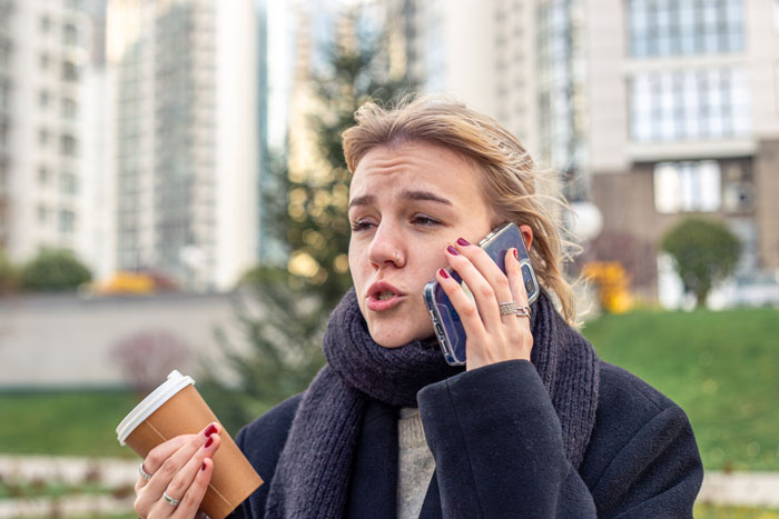 Woman talking on phone outdoors, holding a coffee cup, depicting aunt flipping the script on sticky-fingers niece scenario. Woman talking on phone outdoors, holding a coffee cup, depicting aunt flipping the script on sticky-fingers niece scenario.