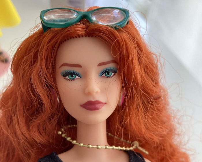 Customized doll with red hair, wearing green glasses and a gold necklace, symbolizing creativity and personalization. Customized doll with red hair, wearing green glasses and a gold necklace, symbolizing creativity and personalization.