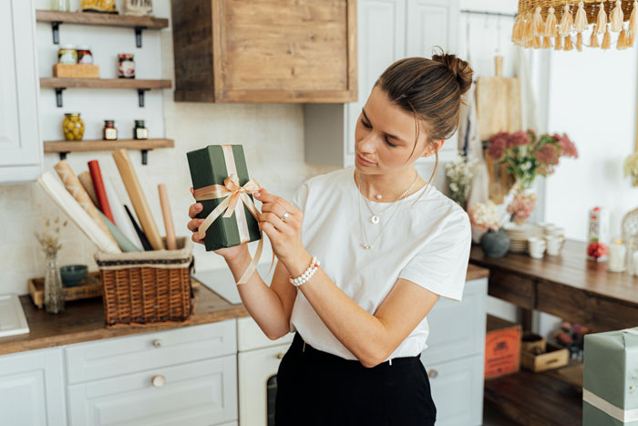 Woman in a kitchen, examining a gift box with a ribbon, symbolizing a customized doll for a young child. Woman in a kitchen, examining a gift box with a ribbon, symbolizing a customized doll for a young child.