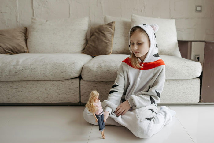 Child in animal onesie sitting on floor, holding a doll, by a couch. Child in animal onesie sitting on floor, holding a doll, by a couch.