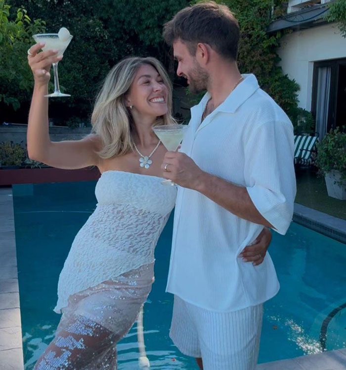 Bride smiling in a lace dress, holding a cocktail with groom by pool, showcasing a fun wedding moment. Bride smiling in a lace dress, holding a cocktail with groom by pool, showcasing a fun wedding moment.