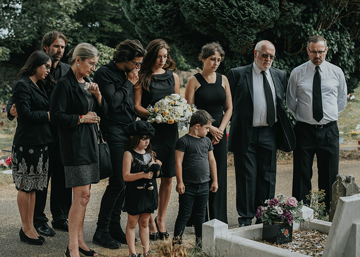 A group of mourners, including children, solemnly gathered at a funeral, reflecting on hidden childhood trauma.