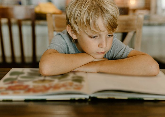 Young boy thoughtfully looking at a book, reflecting on childhood experiences that might have been traumatic.