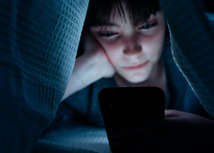 Child under blanket, focused on phone screen at night, reflecting childhood experiences and trauma.