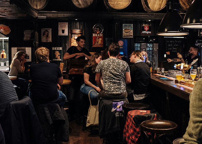 People socializing in a dimly lit bar, surrounded by vintage beer posters and barrels.