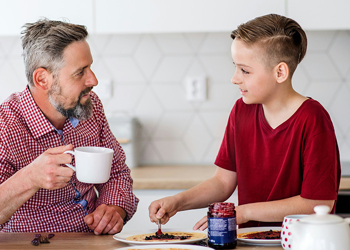 Father and son having breakfast in the kitchen, dad holding a coffee cup, highlighting childhood experiences.