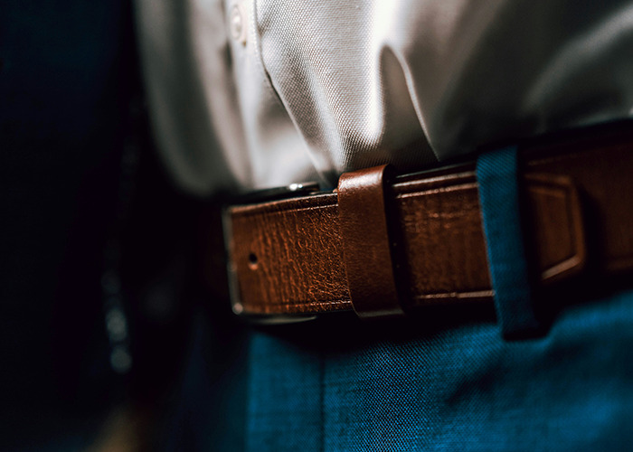 Close-up of a brown leather belt on a person's waist, symbolizing childhood experiences.