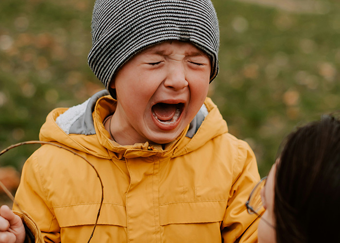 A child in a striped hat and yellow coat crying outdoors, reflecting childhood trauma experiences.