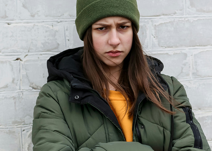 Young person in a green jacket and beanie, looking serious, symbolizing experiences that seemed normal but were traumatic.