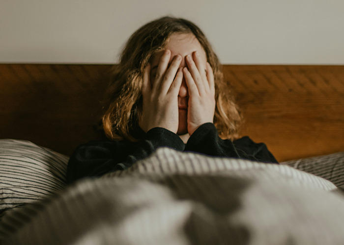 Child hiding face in bed, illustrating childhood trauma experiences.
