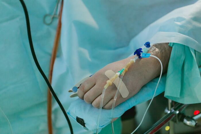 Patient's hand with IV in hospital setting, representing hospital workers sharing patient regrets.
