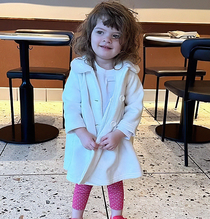 A young girl in a white coat and pink leggings smiles indoors, linked to a tragic hot car incident. A young girl in a white coat and pink leggings smiles indoors, linked to a tragic hot car incident.