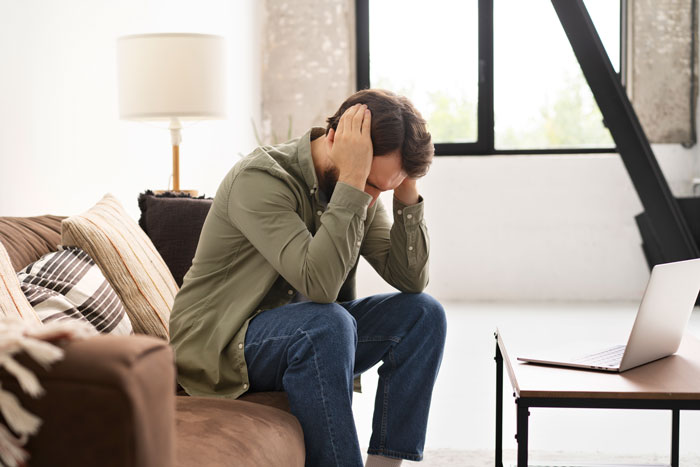 Man sitting on a couch, holding his head in his hands, appearing stressed about decision regarding kids. Man sitting on a couch, holding his head in his hands, appearing stressed about decision regarding kids.