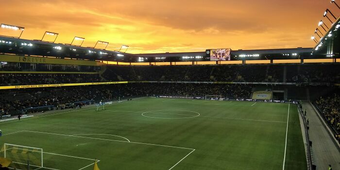 A large soccer stadium filled with fans under a vibrant sunset sky, a true cathedral of soccer history.