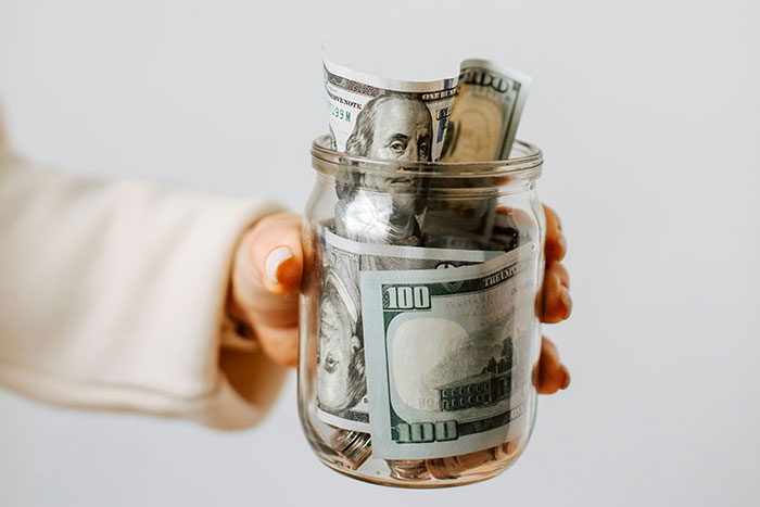 A hand holding a jar filled with U.S. dollar bills, representing the financial habits of older generations.
