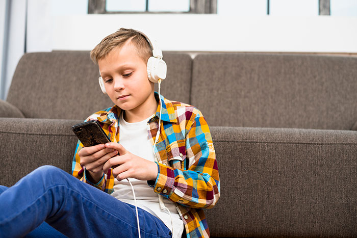 A young boy with headphones, using a smartphone, representing modern tech influence on younger generations.