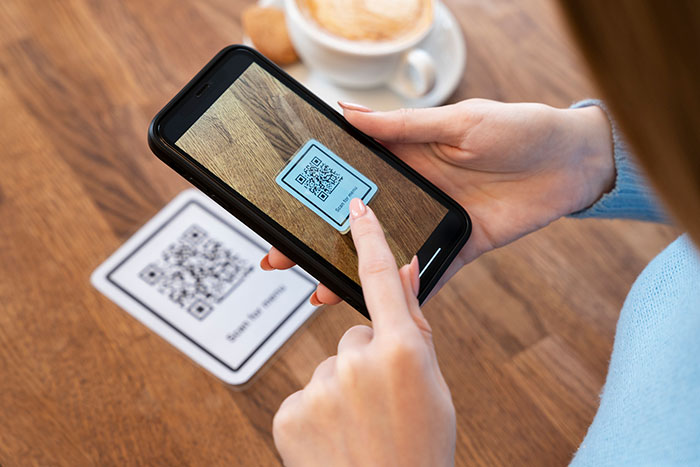 Person scanning QR code on phone at a cafe table, representing a boomer-approved habit.