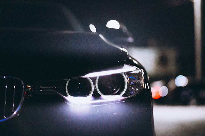Close-up of a car's headlight at night, highlighting the sleek design admired by older generations.