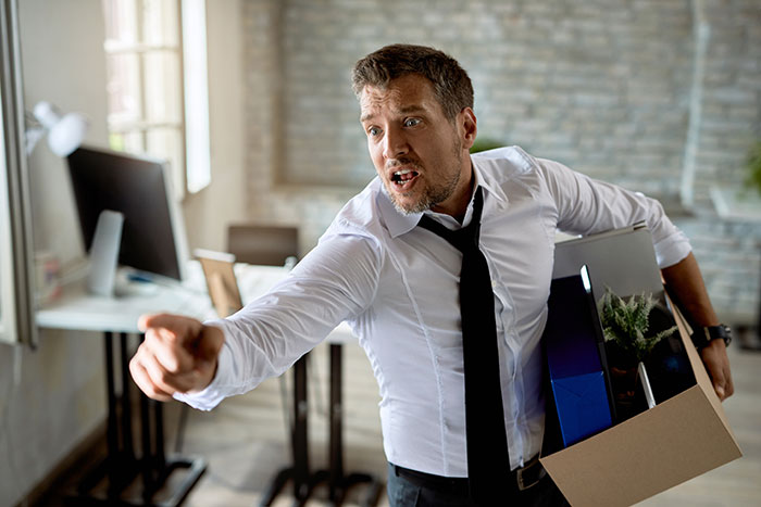 Man in office holding a box, pointing angrily; illustrates company firing scenario. Man in office holding a box, pointing angrily; illustrates company firing scenario.