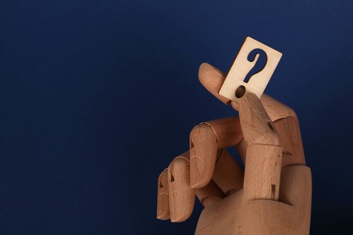 Wooden hand holding a question mark against a dark blue background, symbolizing the Mandela Effect challenge. Wooden hand holding a question mark against a dark blue background, symbolizing the Mandela Effect challenge.