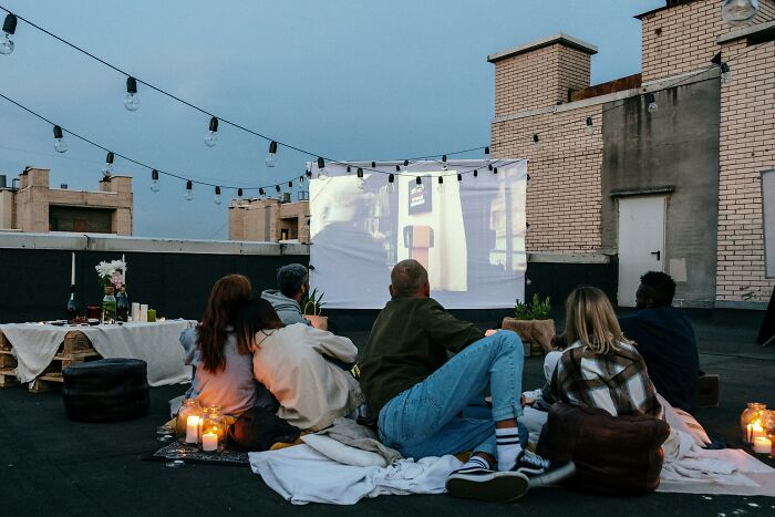 People watching a film scene outdoors on a rooftop, seated on blankets with soft lighting, reminiscent of another movie. People watching a film scene outdoors on a rooftop, seated on blankets with soft lighting, reminiscent of another movie.