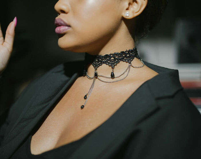 Person wearing a black choker with chains, dressed informally in a blazer at work.