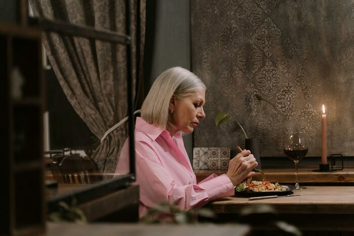 A woman in a pink shirt enjoying a meal alone at a candlelit dinner table.