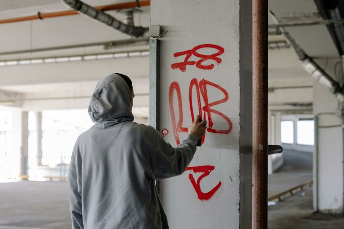 Person in a hoodie spray-painting graffiti on a wall, illustrating how society normalizes unusual behaviors.