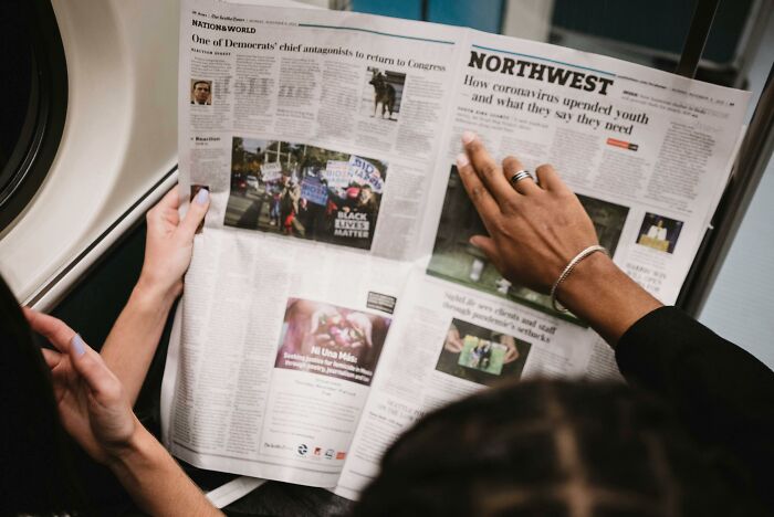 People reading a newspaper together, hands turning the pages, discussing an insignificant thing.
