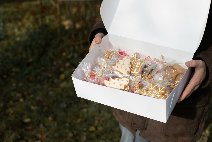 Person holding a white box of decorated cookies, reminiscent of adult experiences of being picked last.
