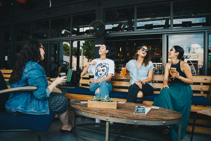 Four friends laughing and enjoying drinks at an outdoor patio, sharing adult experiences.