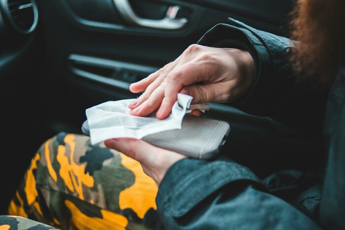 Person cleaning a phone with a wipe, reflecting common modern misconceptions about hygiene practices.