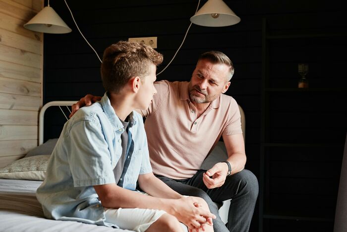 Man and boy on a bed having a serious conversation in a warmly lit room.
