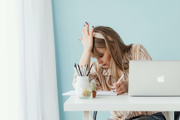 Woman at a desk with a laptop, surrounded by gradually disappeared things, writing thoughtfully.