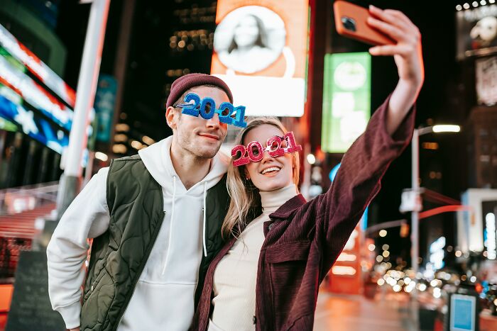 Two people wearing 2021 glasses take a selfie in a vibrant cityscape at night.