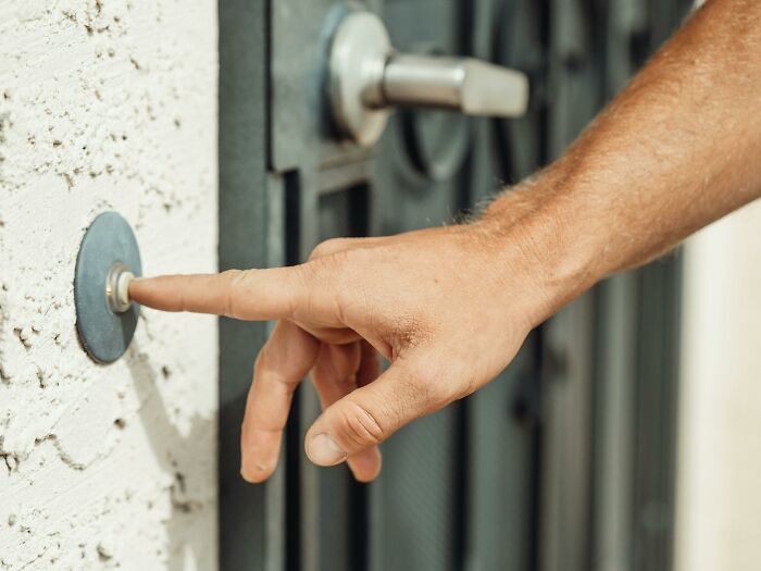 A hand pressing a doorbell, a typical small thing in a middle-class home setting.