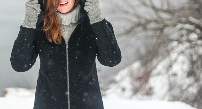 Woman in snowy scene wearing a black coat and gray gloves, symbolizing misconceptions in winter attire choices.