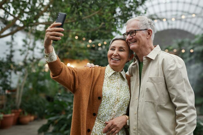 Senior couple smiling and taking a selfie together in a greenhouse, challenging common stereotypes.