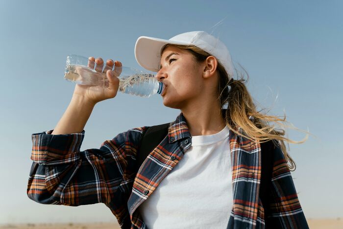 Woman drinking bottled water, thought to be healthy, under a clear blue sky.