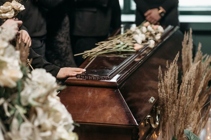 A somber adult experience depicted with a hand resting on a wooden coffin adorned with flowers at a funeral.