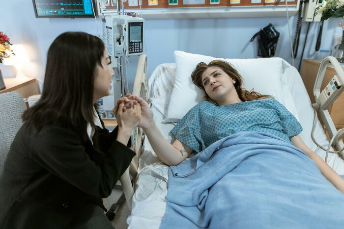 Hospital worker holds a patient's hand in a comforting gesture, sharing moments of reflection and regrets.