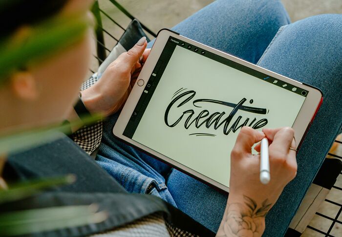 Person using a tablet to write "Creative," symbolizing overused office expressions.