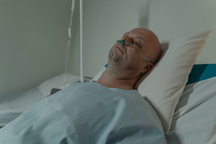 A patient with an oxygen tube in a hospital bed, reflecting on life choices.