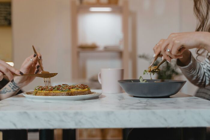 Two people dining at a marble table, experiencing an awkward adult moment, with utensils and plates.